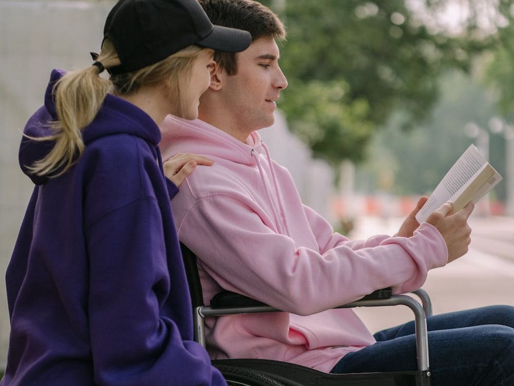 man in wheel chair and woman looking at a book